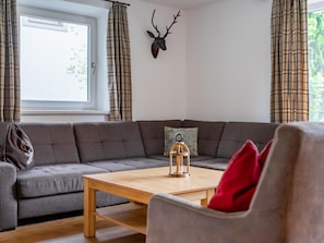 Ein modernes Wohnzimmer mit einem grauen Ecksofa, einem Holztisch und einem aufgehängten Hirschgeweih an der Wand.