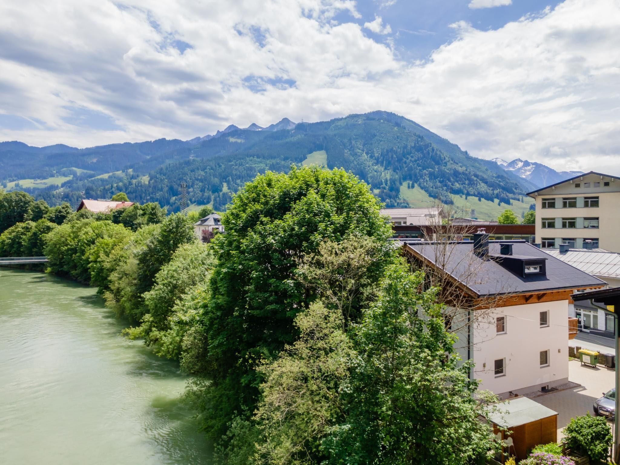 A riverside view with buildings, trees, and mountains in the background.