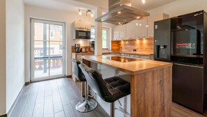 Una cocina moderna con una isla central, taburetes de bar, electrodomésticos de acero inoxidable y vistas a través de un ventanal.