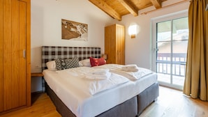 Un dormitorio con techo de madera, una cama con ropa de cama blanca, cabecera escocesa y una ventana con cortinas.