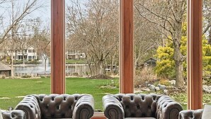 A room with two leather armchairs facing a large window with a view of a lake and trees.