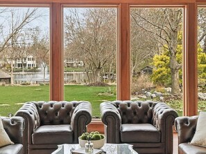 Una habitación con dos sillones de cuero orientados hacia un ventanal con vistas a un lago y árboles.