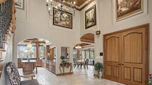 A spacious interior with a grand staircase, a dining area, and a large wooden door.