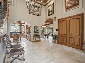 Un interior espacioso con una imponente escalera, un comedor y una puerta grande de madera.
