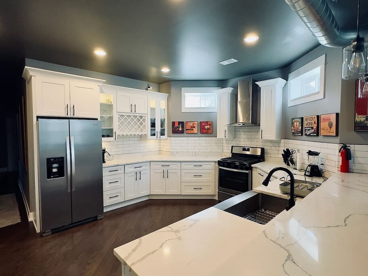 A modern kitchen with white cabinetry, a stainless steel refrigerator, a black faucet, and a marble countertop.