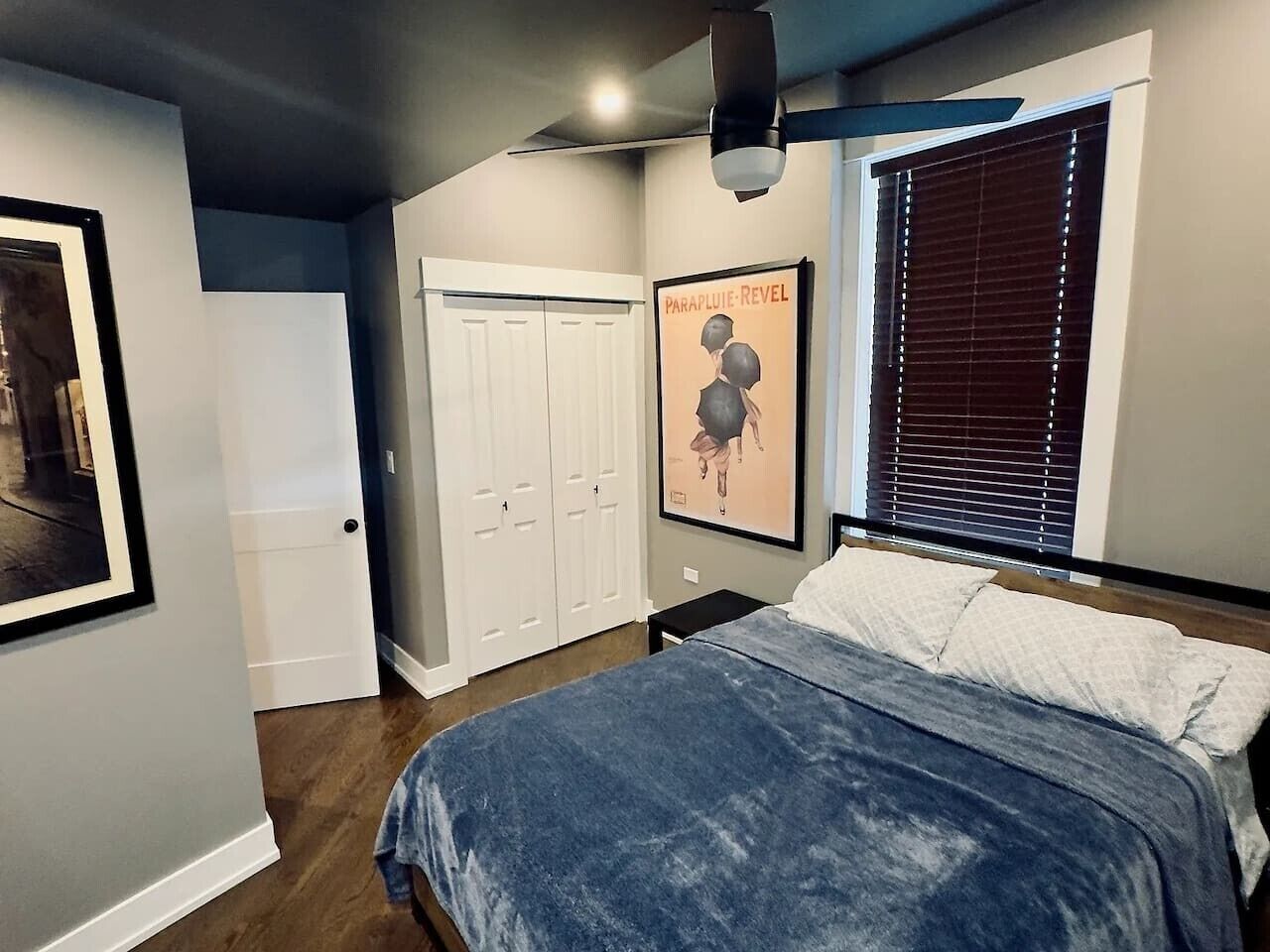 Une chambre à coucher avec un lit, une armoire, une affiche et une fenêtre avec des stores.