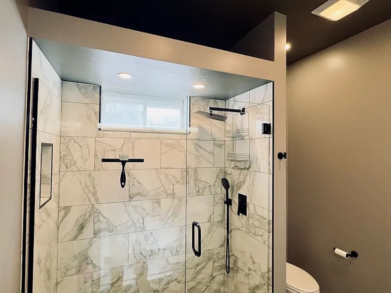 A modern bathroom with a glass-enclosed shower, marble tiles, and a toilet.