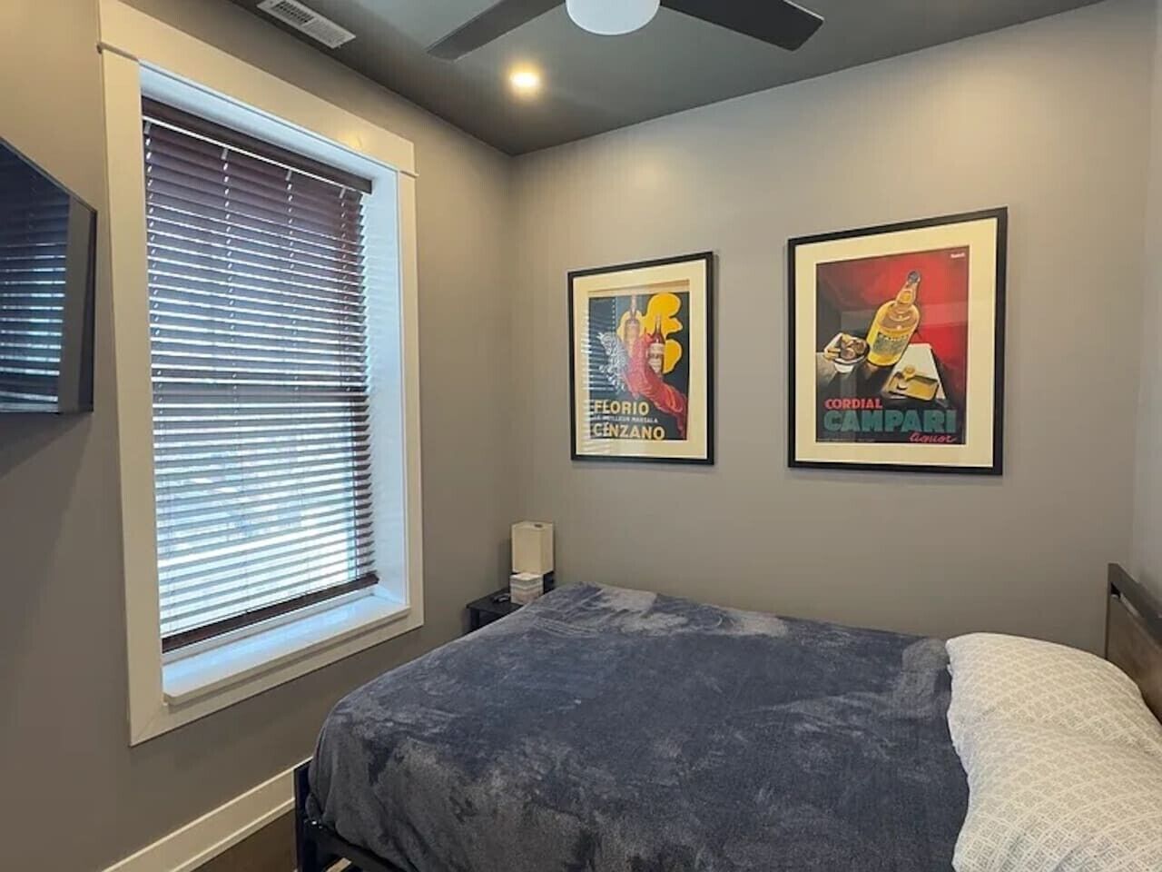 Un dormitorio con cama, ventana con persianas y dos cuadros en la pared.