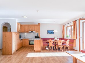 Eine kleine Küche mit Holzausbau, ein Essbereich mit Tisch und Stühlen sowie ein Fenster mit Vorhängen.