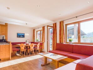 A modern living room with a sofa, dining table, chairs, and a kitchen area with wooden cabinets and a television. - Holiday Apartment with a spa next to the gondola (Brixen im Thale)