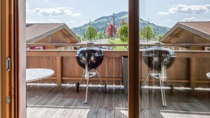An outdoor deck with two barbecue grills, wooden fencing, and a view of a mountainous landscape. - Luxury apartment with wellness next to gondola (Brixen im Thale)