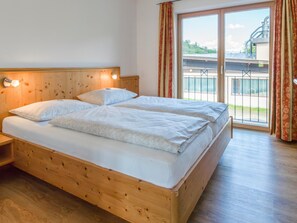 A double bed with a wooden headboard, a nightstand, and a large window with curtains. - Luxury apartment with wellness next to gondola (Brixen im Thale)