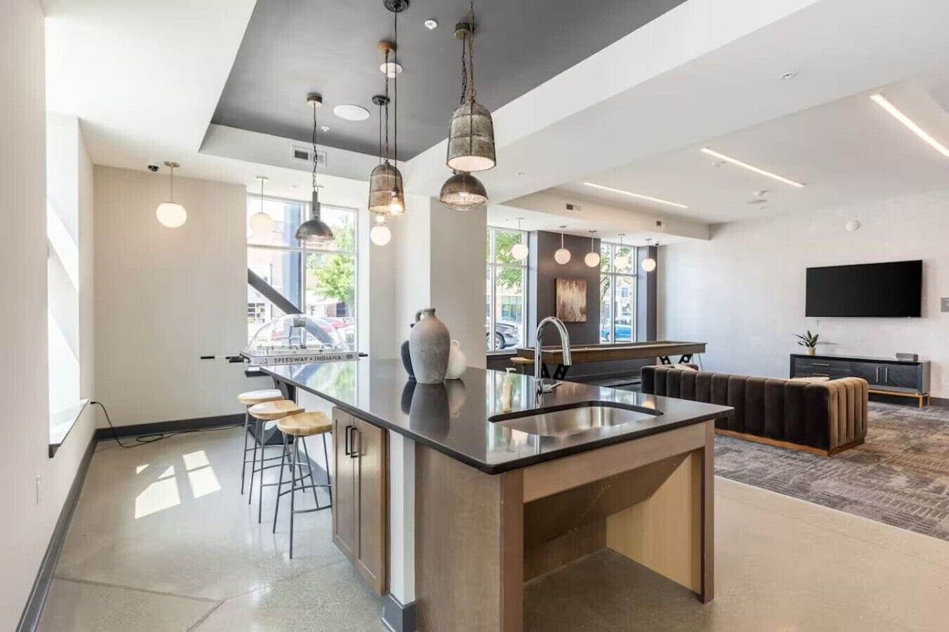 Een moderne keuken met een centraal eiland, hangende lampen en een groot raam.