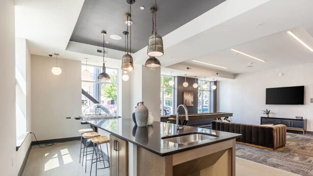A modern kitchen with a central island, pendant lighting, and a large window. - Fast Lane Flat: Walk to Track, Dining & Parking (Speedway)