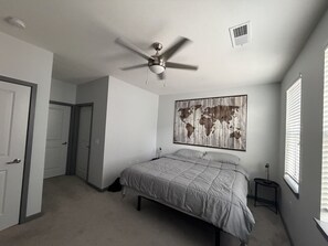 Ein Schlafzimmer mit einem Bett, einem Deckenventilator, einem Wandbild, einem Fenster mit Jalousien und einer Tür.