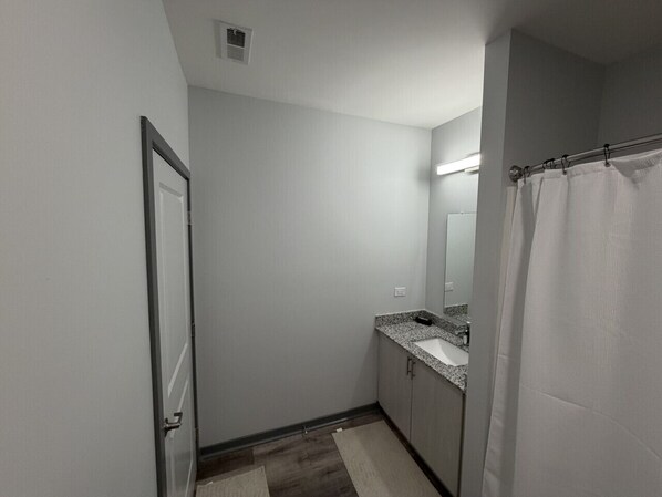Un baño con puerta, lavamanos, espejo y cortina de ducha.