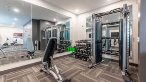A gym with exercise equipment, mirrors, and a wall-mounted TV. - Fast Lane Flat: Walk to Track, Dining & Parking (Speedway)