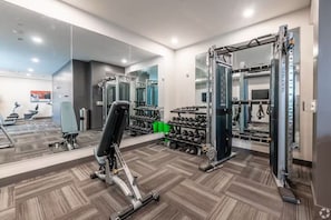 Ein Fitnessraum mit Trainingsgeräten, Spiegeln und einem an der Wand befestigten Fernseher.