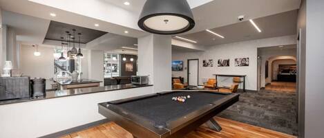 A modern indoor pool area with a pool table, seating, and a bar area.