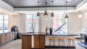 A modern kitchen with a central island, bar stools, pendant lighting, and a coffee machine. - Fast Lane Flat: Walk to Track, Dining & Parking (Speedway)
