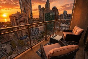 Un balcón con muebles de mimbre, vistas a un paisaje urbano al atardecer y edificios altos.