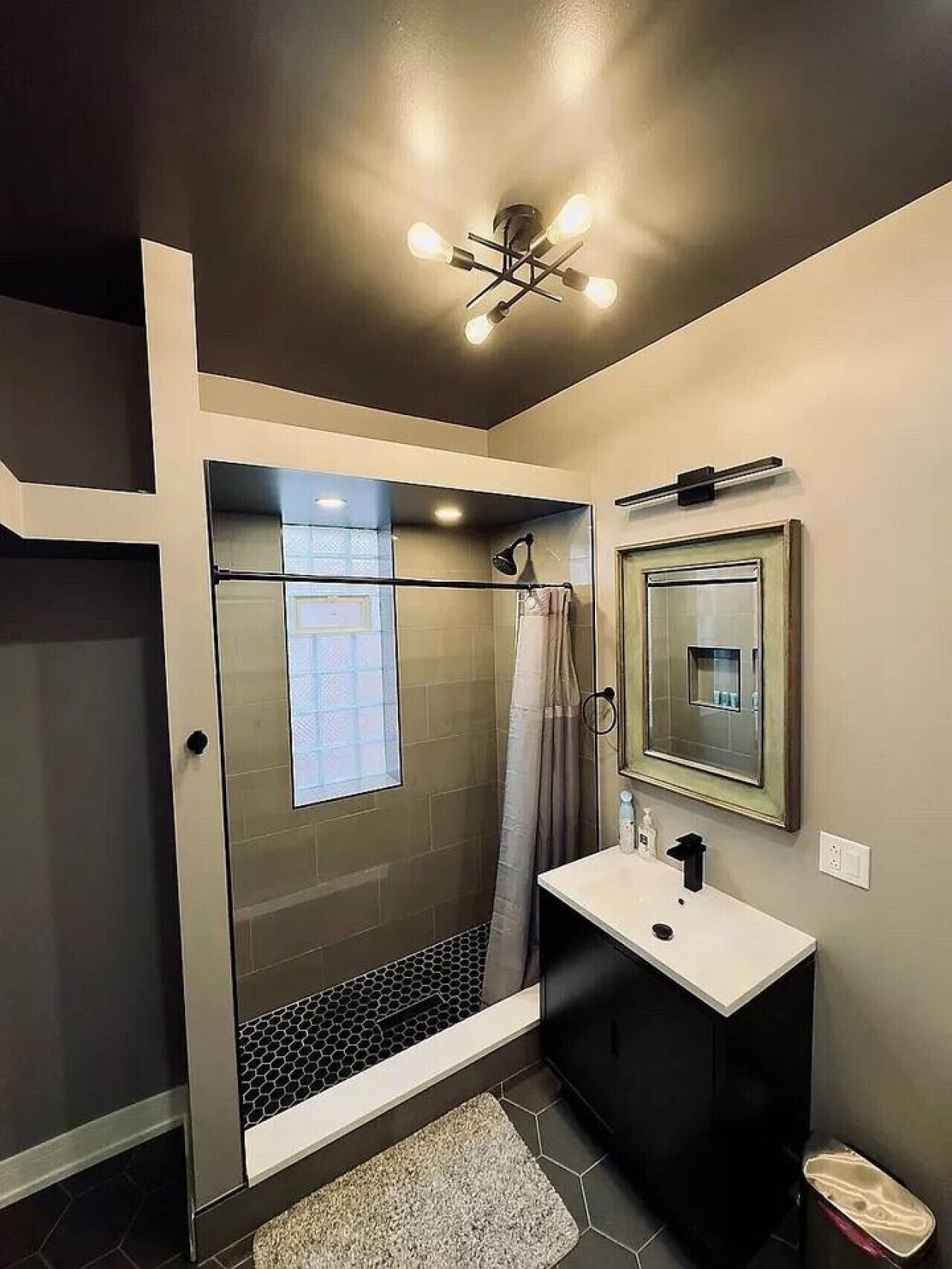 A modern bathroom with a glass-enclosed shower, a white sink, and a mirror above it.
