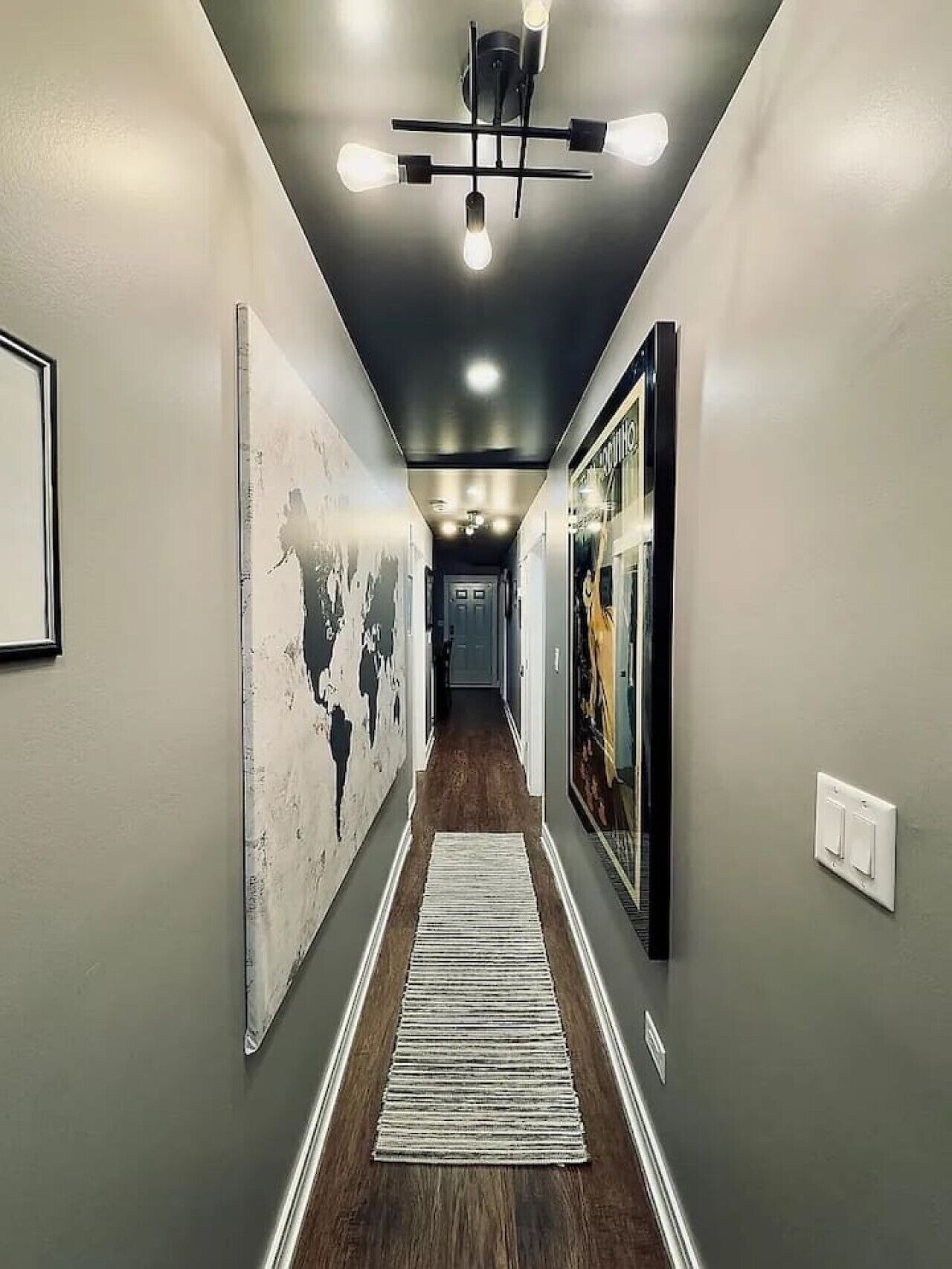 A hallway with a wooden floor, a white rug, and framed artwork on the walls.
