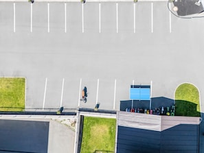 Ein Luftbild eines Parkplatzes mit markierten Stellplätzen, einem Gebäude mit blauer Tür und einem eingezäunten Bereich mit farbigen Objekten.