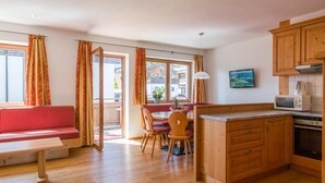 A cozy living area with a wooden bench, a dining table with chairs, a kitchen with wooden cabinets and appliances, and a sliding glass door leading to an outdoor area. - Luxury apartment with spa next to the gondola (Brixen im Thale)