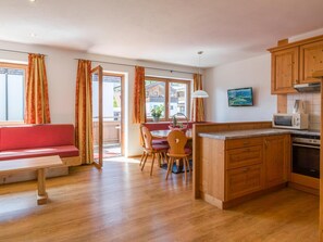 A cozy living area with a wooden bench, a dining table with chairs, a kitchen with wooden cabinets and appliances, and a sliding glass door leading to an outdoor area. - Luxury apartment with spa next to the gondola (Brixen im Thale)