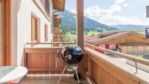A balcony with a barbecue grill, wooden railings, and a view of mountains. - Luxury apartment with spa next to the gondola (Brixen im Thale)