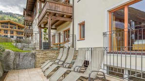 A terrace with lounge chairs, a stone wall, and a view of a mountain. - Luxury apartment with a spa next to the gondola (Brixen im Thale)
