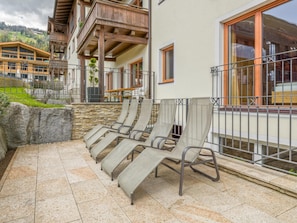 Eine Terrasse mit Liegestühlen, einer Steinsäule und Blick auf einen Berg.