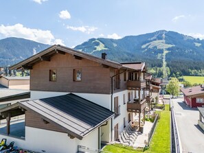 A multi-story building with balconies, a covered outdoor seating area, and a view of mountains. - Luxury apartment with a spa next to the gondola (Brixen im Thale)