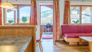 A room with a wooden dining table, a red sofa, and a view of a mountainous landscape through large windows. - Luxury apartment with a spa next to the gondola (Brixen im Thale)