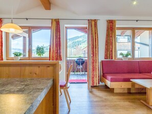 A room with a wooden dining table, a red sofa, and a view of a mountainous landscape through large windows. - Luxury apartment with a spa next to the gondola (Brixen im Thale)