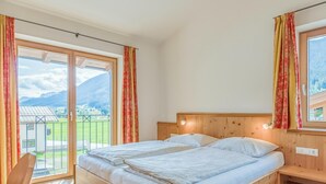 A bedroom with a wooden bed, a nightstand, and a view of a mountainous landscape through large windows. - Luxury apartment with a spa next to the gondola (Brixen im Thale)
