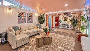 Un salon moderne avec un canapé d’angle, une table basse et un coin repas comprenant une table et des chaises blanches.