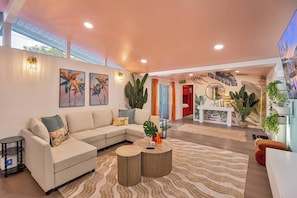 A modern living room with a sectional sofa, a coffee table, and a dining area with a white table and chairs. - Bright Anaheim Escape | Pool + Backyard Fun (Anaheim)