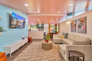 A modern living room with a sofa, a coffee table, a TV, and a kitchen in the background. - Bright Anaheim Escape | Pool + Backyard Fun (Anaheim)