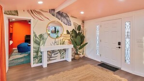 Un couloir avec une console blanche, une grande plante en pot et une porte ornée de panneaux de verre décoratifs.