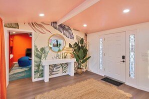 A hallway with a white console table, a large potted plant, and a door with decorative glass panels. - Bright Anaheim Escape | Pool + Backyard Fun (Anaheim)