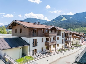 A multi-story hotel with balconies, a covered outdoor area, and a mountainous backdrop. - Deluxe apartment with spa next to the gondola (Brixen im Thale)