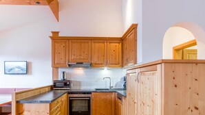A kitchen with wooden cabinets, a microwave, an oven, and a sink. - Deluxe apartment with spa next to the gondola (Brixen im Thale)