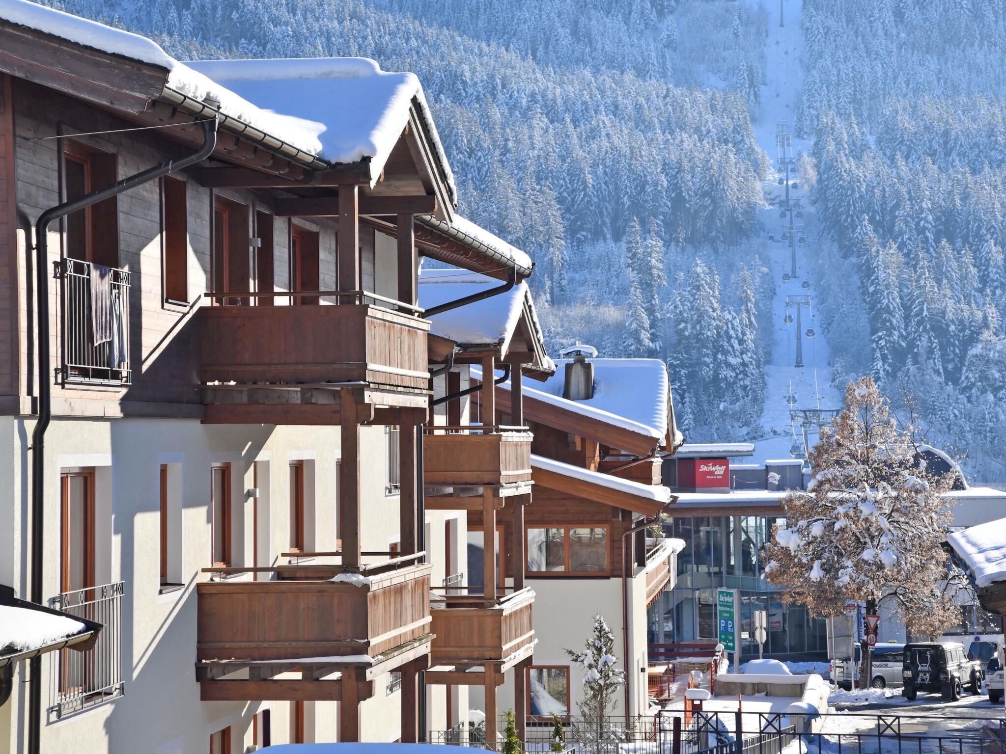A multi-story building with wooden balconies, a ski lift in the background, and a snow-covered mountain.
