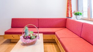 A red sofa, a wooden table, and a wicker basket with fruits. - Deluxe apartment with spa next to the gondola (Brixen im Thale)
