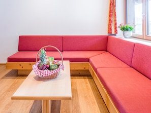 A red sofa, a wooden table, and a wicker basket with fruits. - Deluxe apartment with spa next to the gondola (Brixen im Thale)