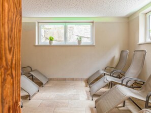 Une salle d’attente avec des chaises, une fenêtre ornée de plantes et un sol carrelé.