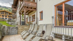 A terrace with lounge chairs, a stone wall, and a view of a mountain. - Deluxe apartment with spa next to the gondola (Brixen im Thale)