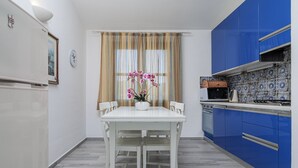 Una cocina con armarios azules, una mesa blanca y un ventanal con cortinas.